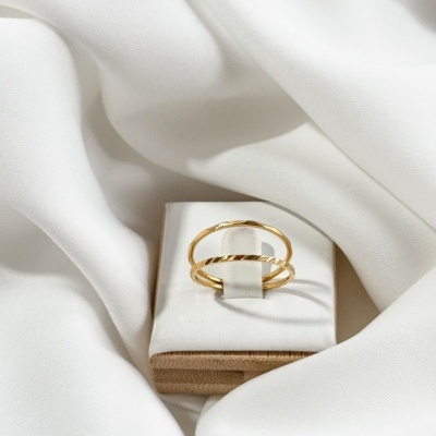 Anel dourado com dois arcos sobre almofada branca e tecido branco