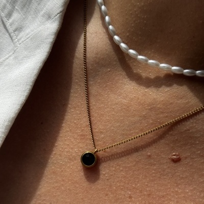 Colar dourado com pendente preto e colar de pérolas ovais brancas no pescoço