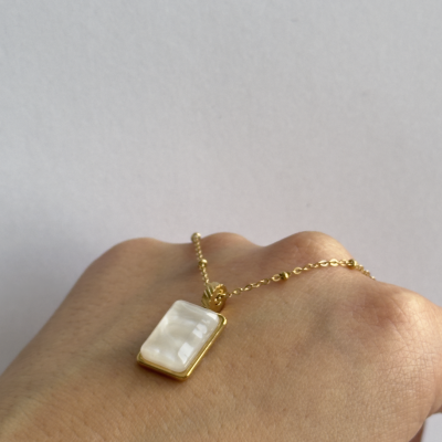 Colar com pendente branco e dourado sobre mão