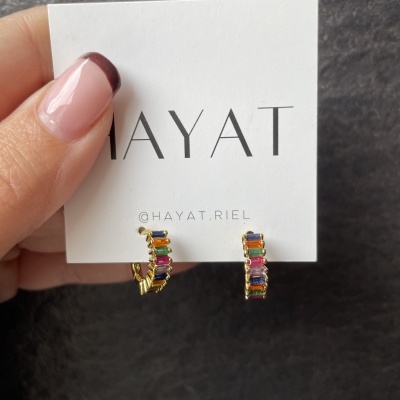 Brincos dourados com pedras coloridas em cartão branco com texto HAYAT e @HAYAT.RIEL