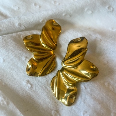 Brincos dourados de metal com formato de asas de borboleta sobre tecido branco texturizado