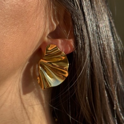 Brinco dourado ondulado na orelha de mulher com cabelo castanho