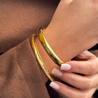 Duas pulseiras douradas num pulso com fundo castanho.
