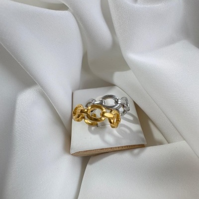 Anéis dourado e prateado em elos grandes sobre suporte branco com tecido branco de fundo