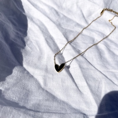 Colar dourado com pendente coração preto sobre tecido branco