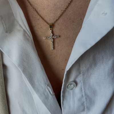 Colar dourado com cruz de pedras sobre camisa branca