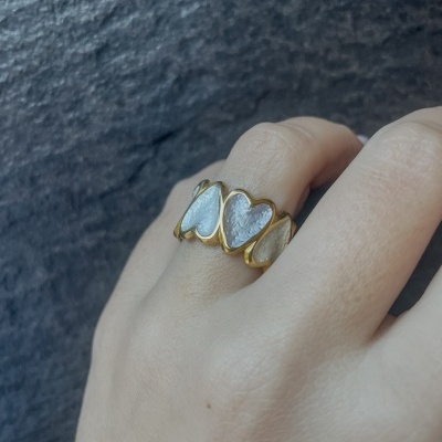 Anel dourado com corações brancos texturizados em dedo feminino.