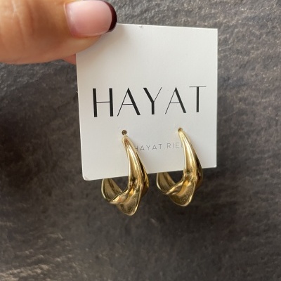 Brincos dourados torcidos em cartão branco da marca HAYAT