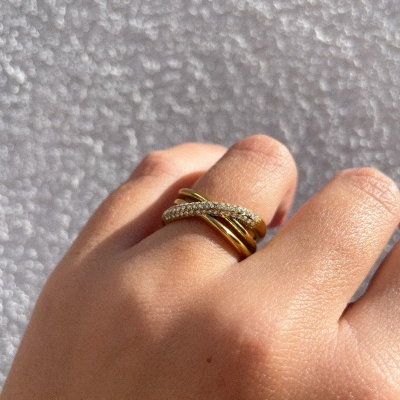 Anel dourado cruzado com cristais num dedo