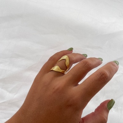 Mão com anel dourado ondulado e unhas verdes sobre fundo branco.