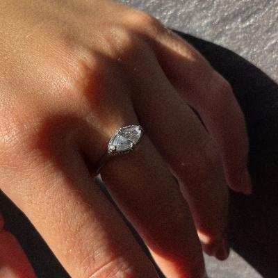 Anel de prata com pedra branca em forma de gota no dedo anelar