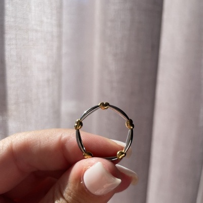 Anel em metal prateado e dourado segurado por mão com unha nude