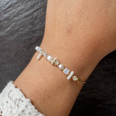 Pulseira delicada com contas brancas, bege e douradas no pulso.