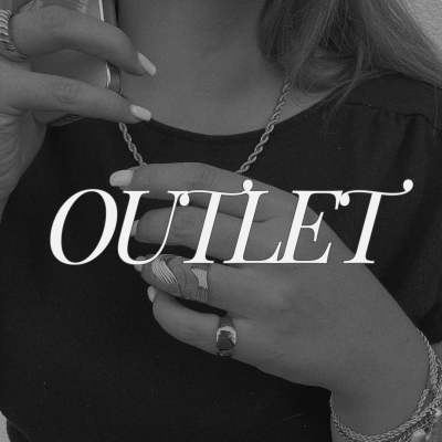 Pessoa usa colar, pulseiras e anéis metálicos em foto preto e branco com roupa preta.