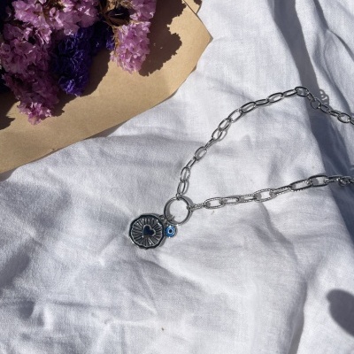 Colar prateado com pendentes e bouquet de flores roxas sobre tecido branco