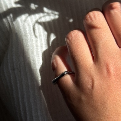 Mão com anel prateado liso sobre tecido branco riscado