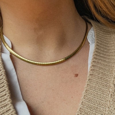 Colar dourado rígido e liso usado no pescoço