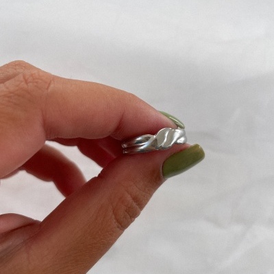 Anel de prata ondulado segurado por mão com unhas verdes