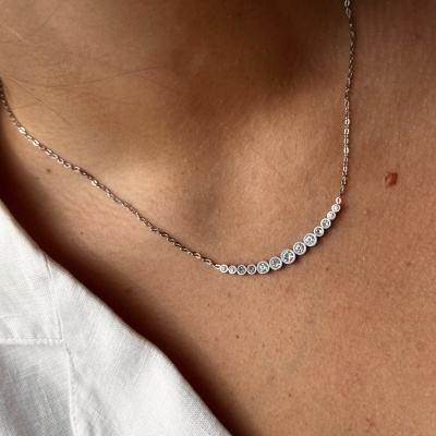 Colar prateado com pedras transparentes de vários tamanhos em curva no pescoço