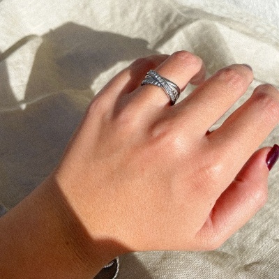 Mão com anel prateado trançado sobre tecido bege