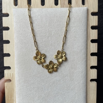 Colar dourado com flores detalhadas pendurado numa placa de madeira claro