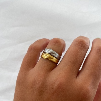 Mão com dois anéis entrelaçados prateado e dourado sobre fundo branco.