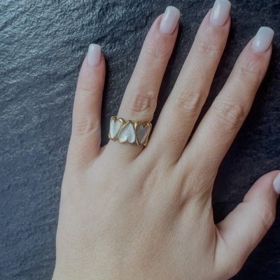 Mão com anel de corações dourado e prateado em fundo preto texturizado