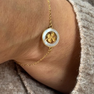 Pulseira dourada com pendente redondo decorativo de flor de quatro folhas no pulso