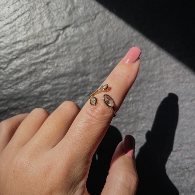 Anel dourado aberto com pedras translúcidas em dedo com unhas rosas