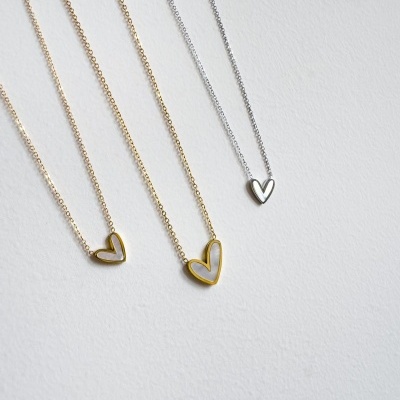 Colares com pendentes em forma de coração dourados e prateado sobre fundo cinza claro