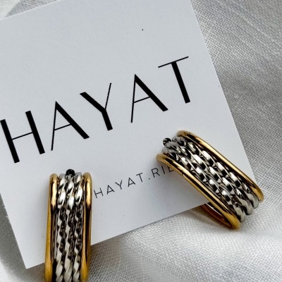 Brincos dourados e prateados trançados sobre cartão branco com texto HAYAT