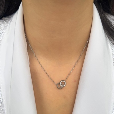 Colar prateado com dois anéis entrelaçados no pescoço de mulher com camisola branca