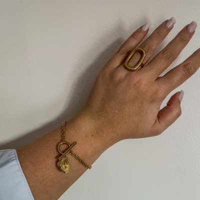 Mão com anel dourado oval e pulseira dourada com pendente