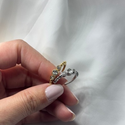 Anéis dourado e prateado com pedras brilhantes em mão feminina sobre tecido branco