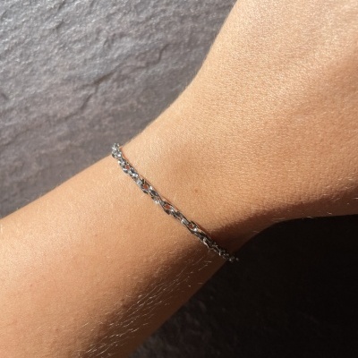 Pulseira prateada fina com elos entrelaçados no pulso