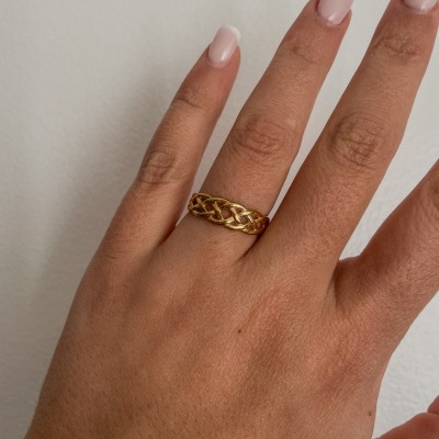 Anel dourado trançado num dedo com unhas pintadas de rosa claro e branco
