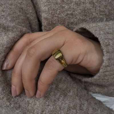Mão feminina com anel dourado largo e camisola castanha de malha