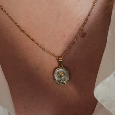 Colar dourado com pendente retangular com desenho de rosa dourada.