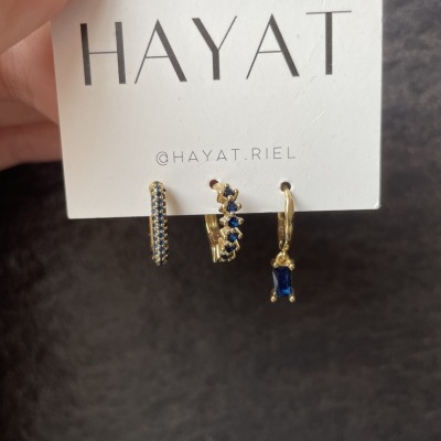 Conjunto de brincos dourados com pedras azuis na embalagem da marca HAYAT