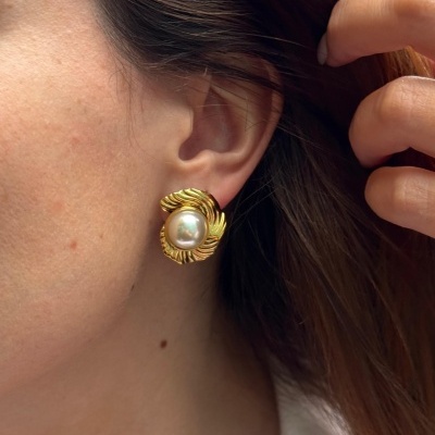 Brinco dourado com pérola central na orelha de mulher