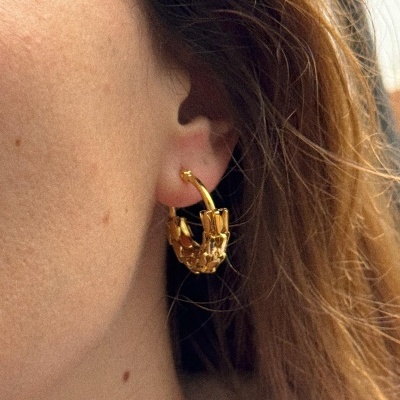 Brinco dourado de argola texturizado na orelha de uma pessoa