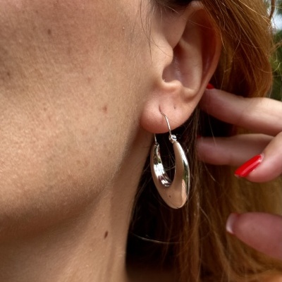 Brincos argola prateada norelha de mulher com unhas vermelhas.