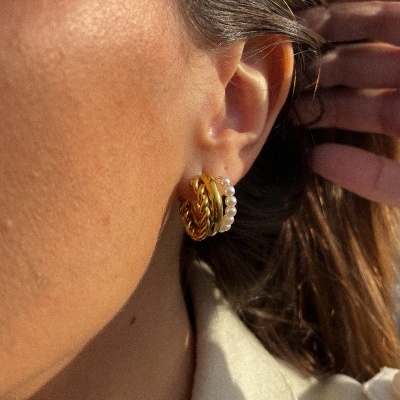 Brincos dourados e pérolas na orelha de uma pessoa