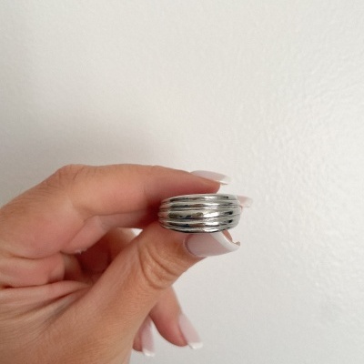 Anel prateado com camadas sendo segurado por mão com unhas brancas