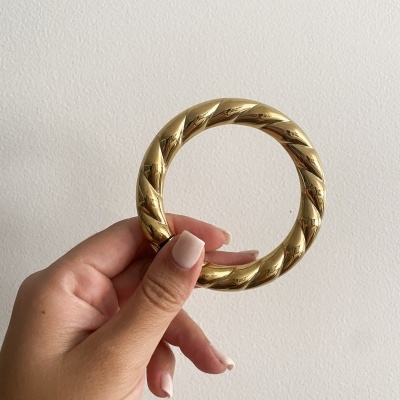 Pulseira dourada em padrão torcido segurada por mão com unhas nude