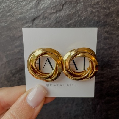 Brincos dourados entrelaçados num cartão branco com texto, fundo escuro.