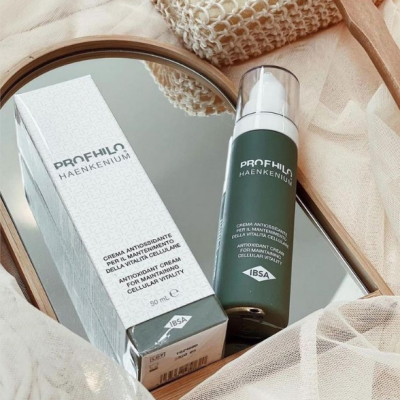 Frasco e caixa de creme Profhilo Haenkenium sobre espelho redondo e tecido bege