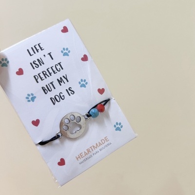 Pulseira preta com pendente de pata de cão em cartão branco com texto e desenhos coloridos