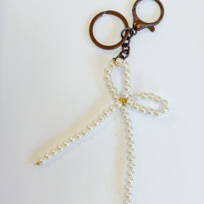 Chaveiro de metal castanho com pingente de conta perolada em fundo branco