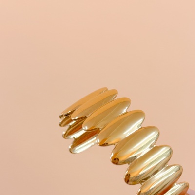 Bracelete dourado ondulado em fundo rosa claro